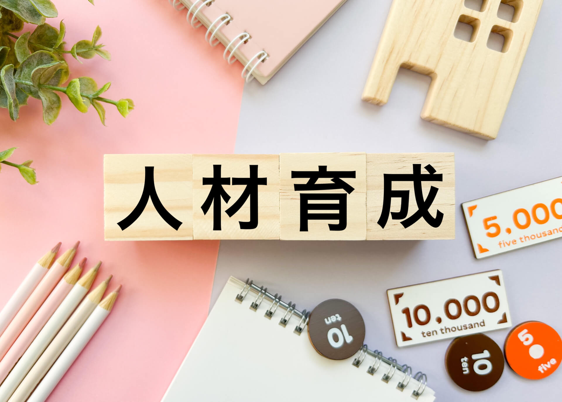 「人材育成」と書かれた木のブロックが並んだ、明るいデスク上のイメージ画像。