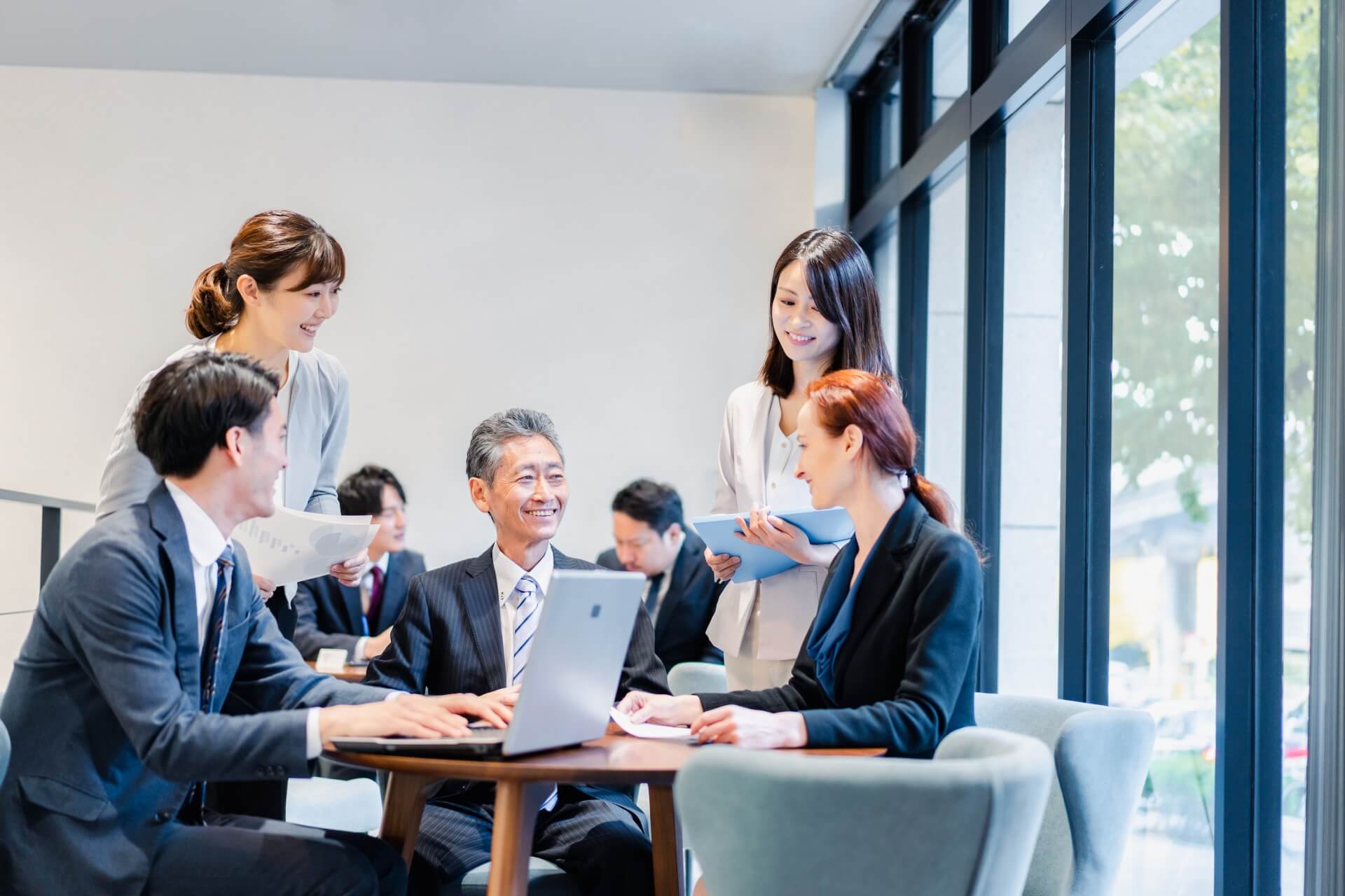 オープンスペースで活発な意見交換をする多様な世代の社員たち。風通しの良い職場の議論風景。