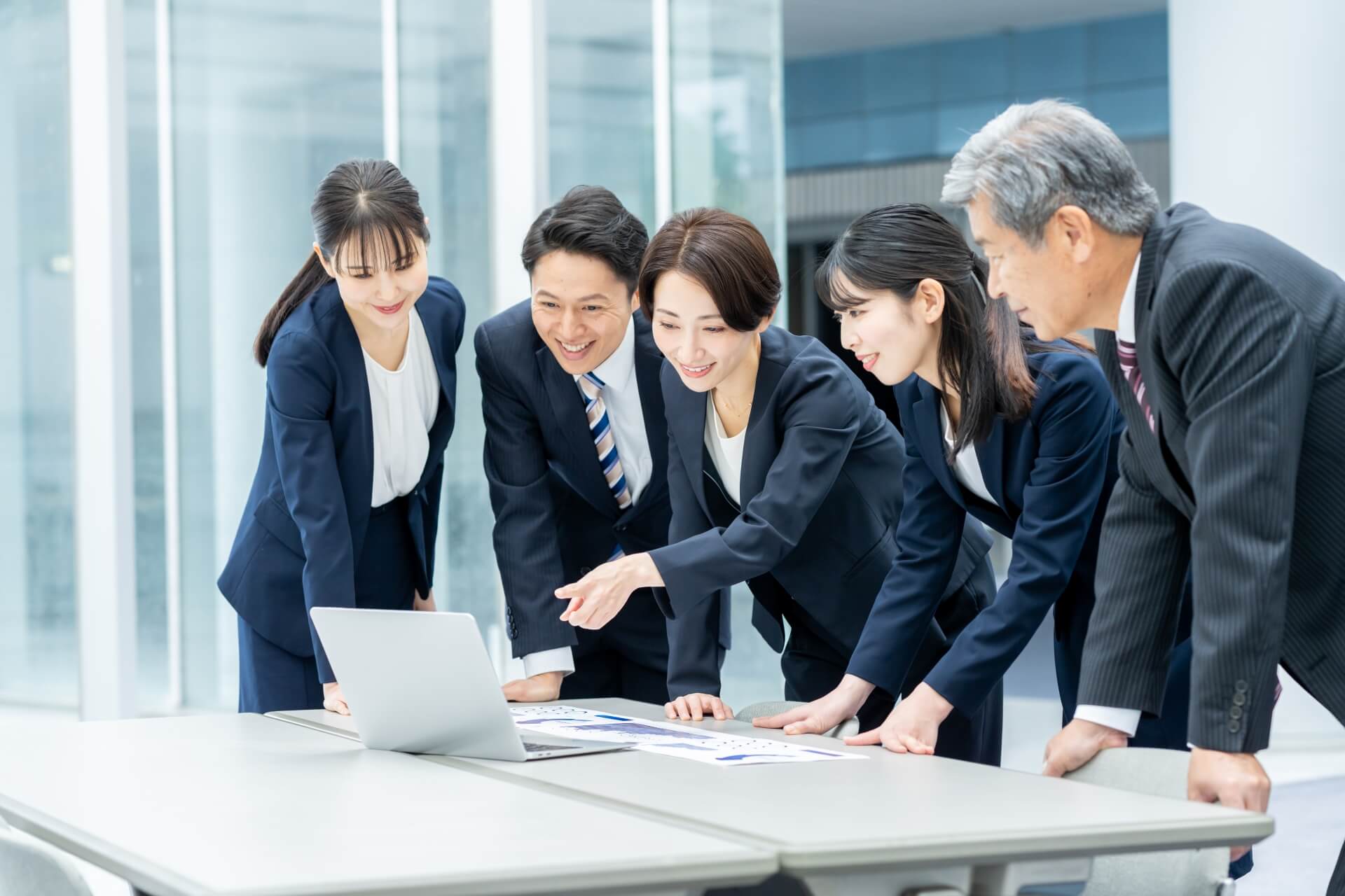 ハイパフォーマー育成に向けた活発なチーム会議風景。多様なビジネスパーソンがPCを囲み、データ分析や戦略について議論する様子