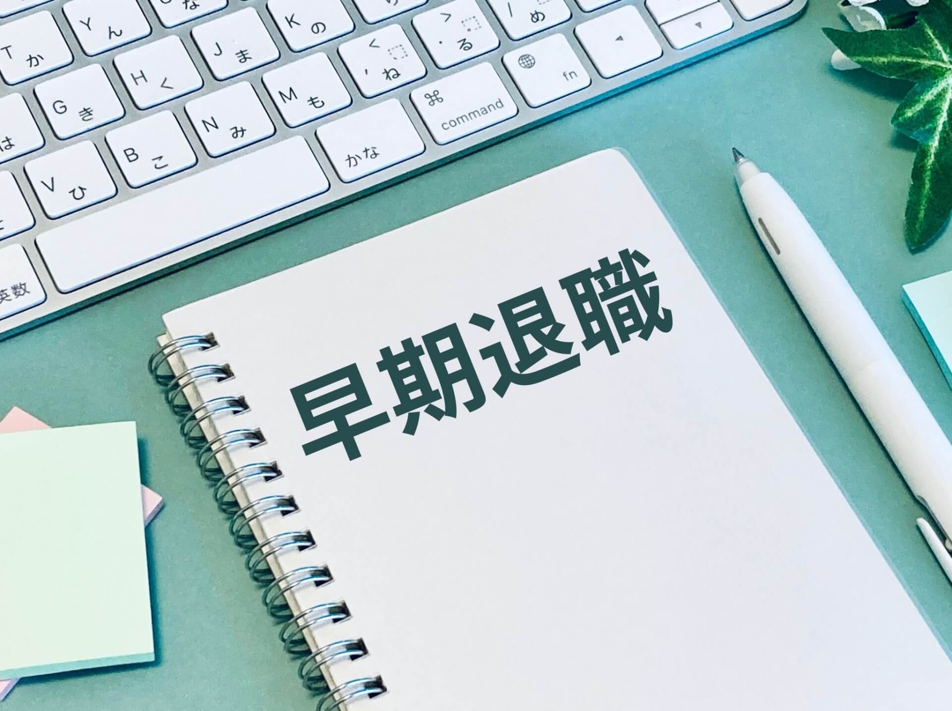 ノートに「早期離職」と書かれた画像。キーボード、ペン、付箋が置かれたビジネスデスクのイメージ。