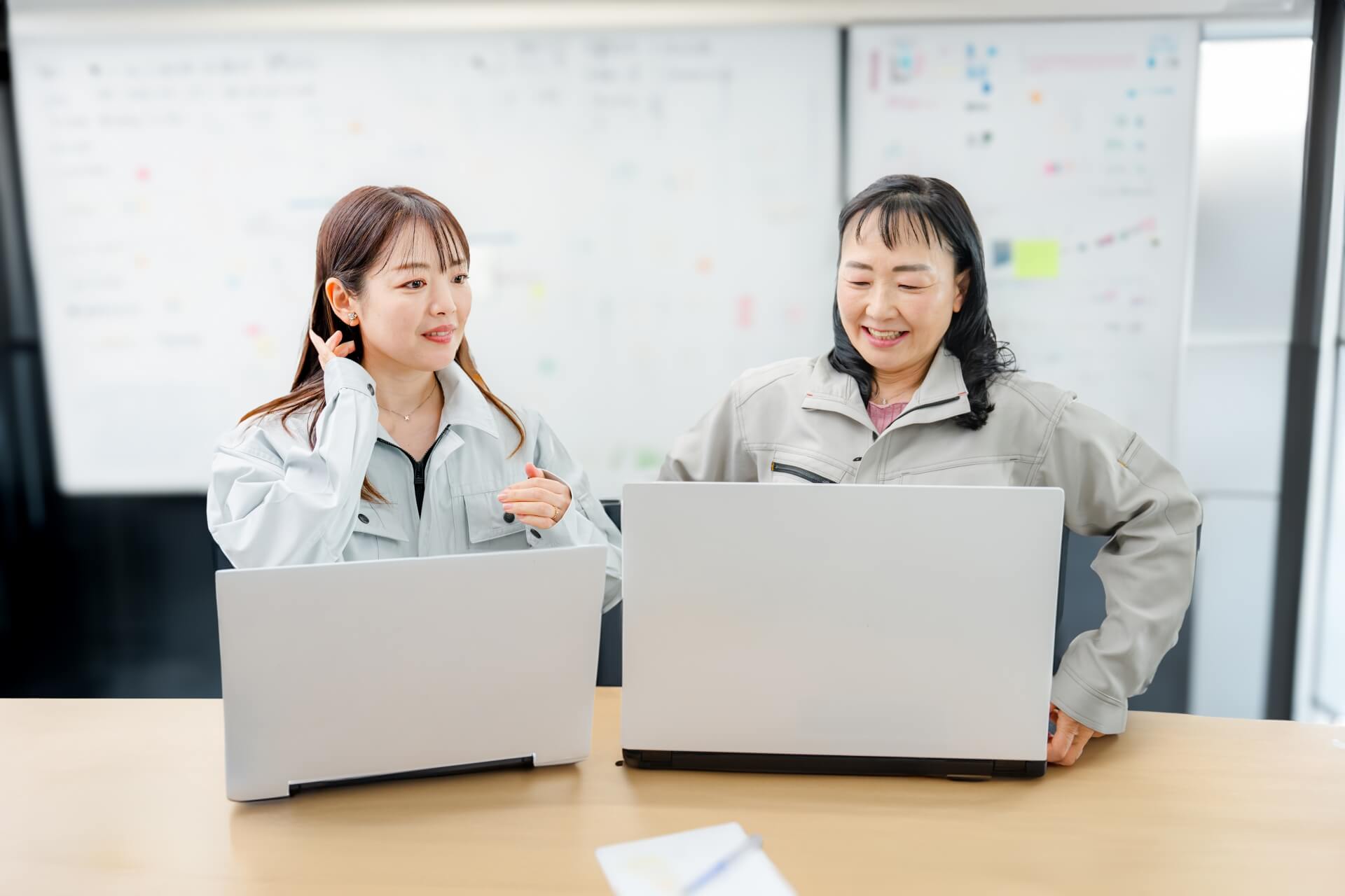 オフィスで作業服を着た女性技術者二人がPCを確認している様子。