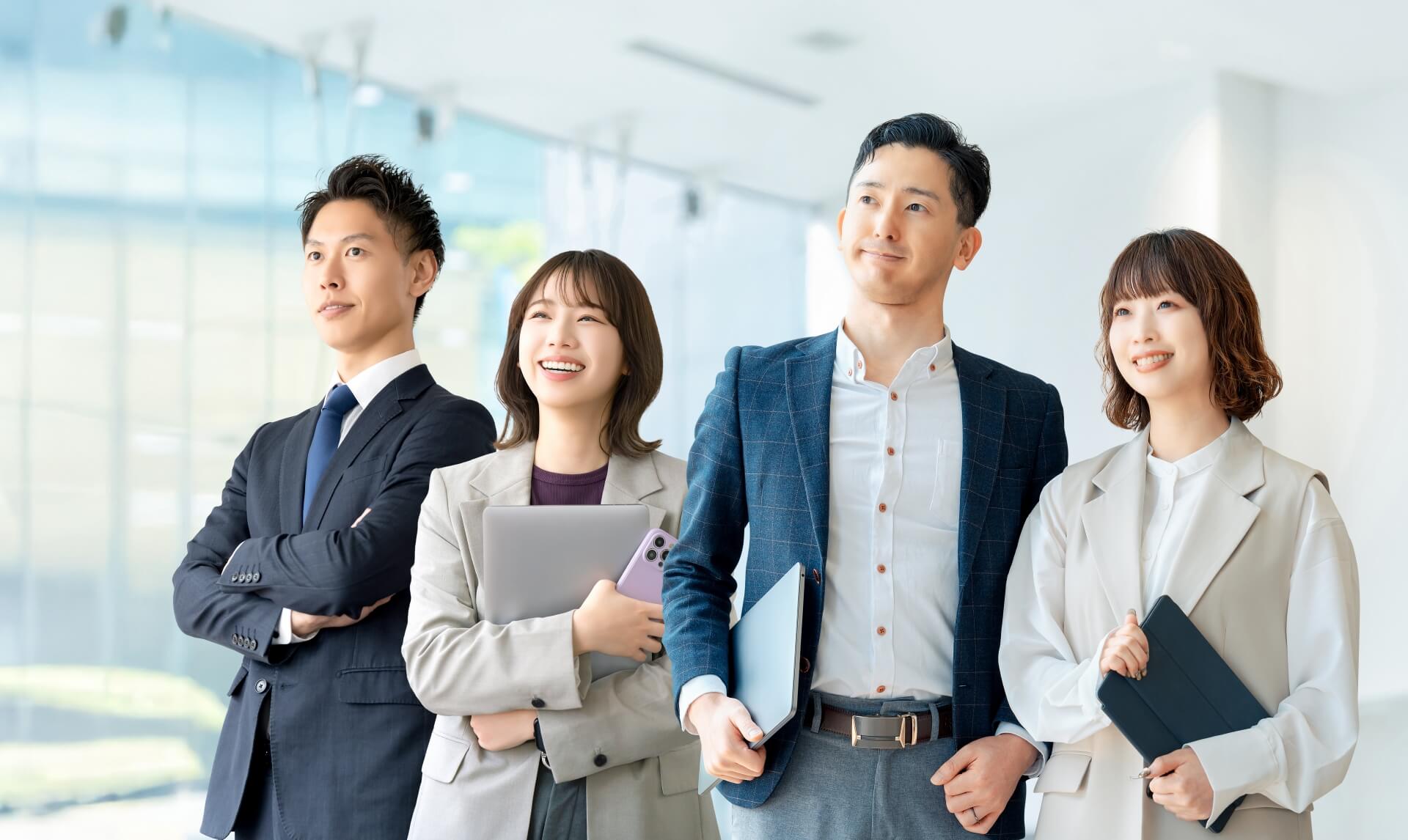 明るいオフィスで自信に満ちた表情で前を見据える4名のビジネスパーソン。チーム全体の高い達成意欲を表現。
