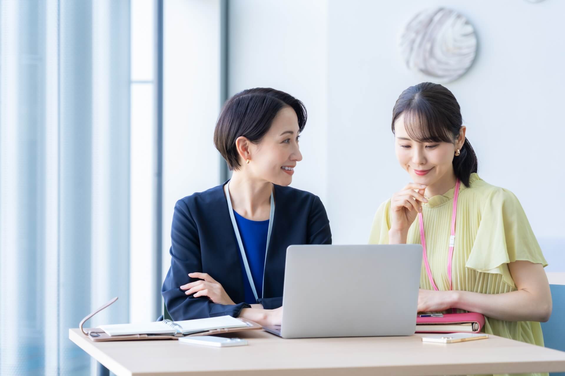 ノートパソコンを見ながら笑顔で対話する女性社員二人