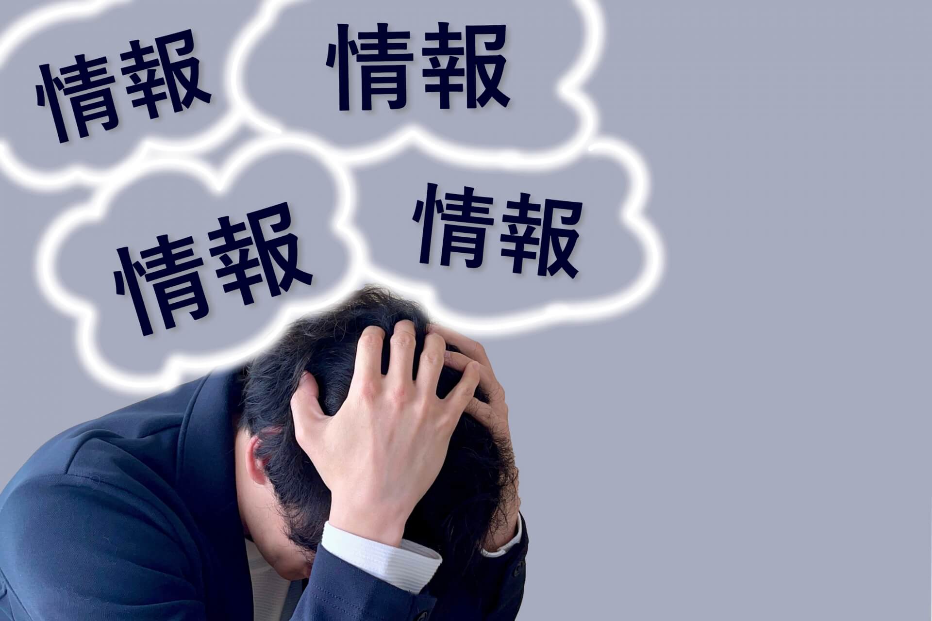 「情報」という文字の吹き出しに囲まれ、頭を抱えて苦悩するスーツ姿の男性